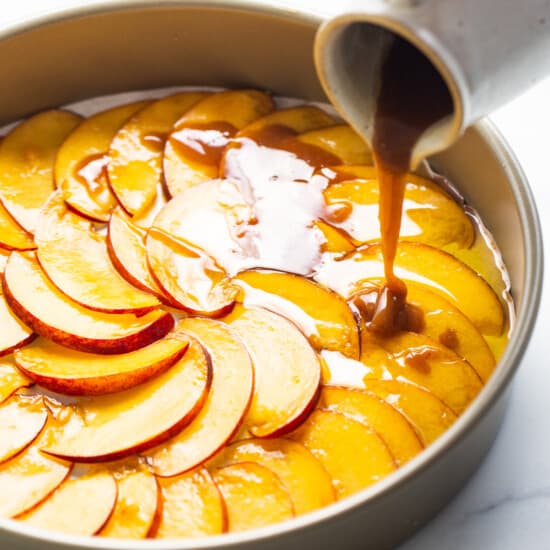 a person pouring caramel over a peach tart in a pan.