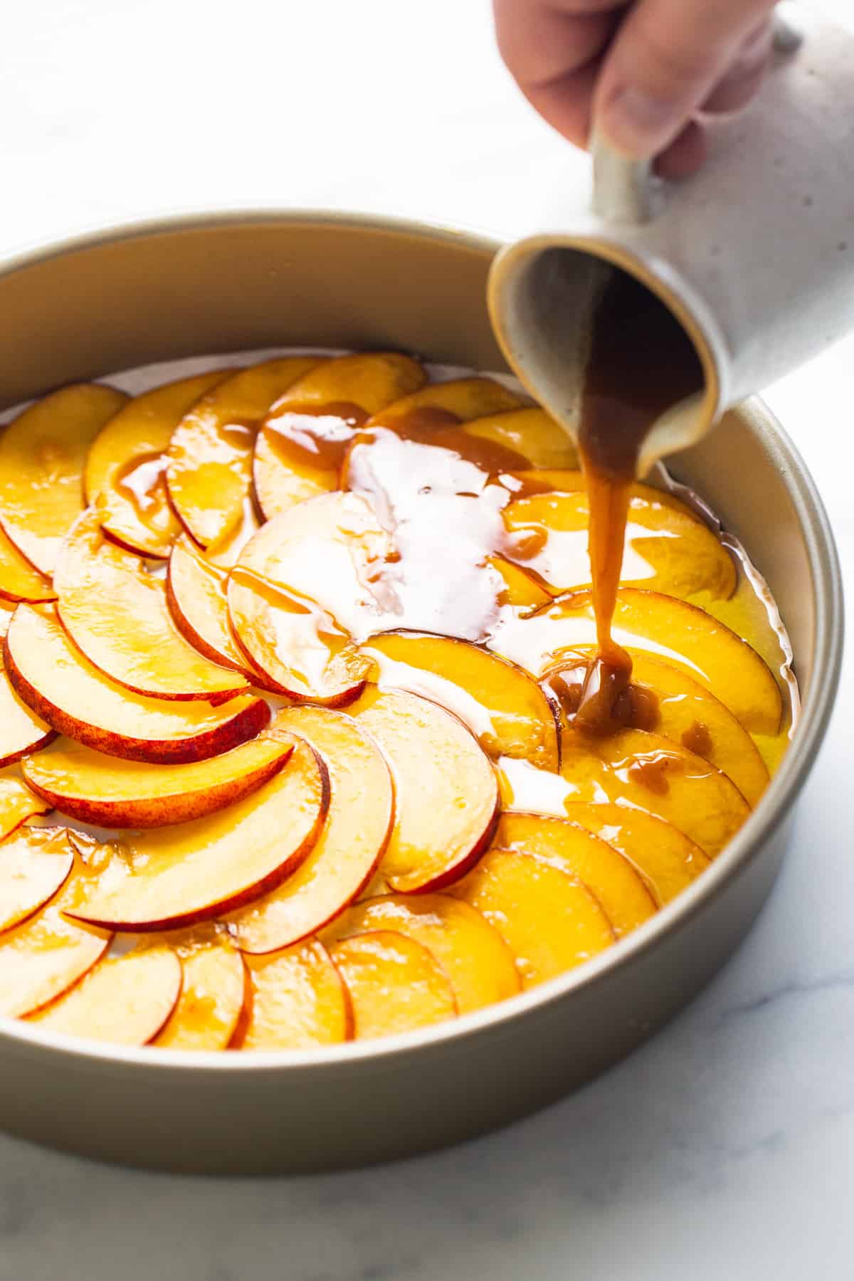 a person pouring caramel over a peach tart in a pan.