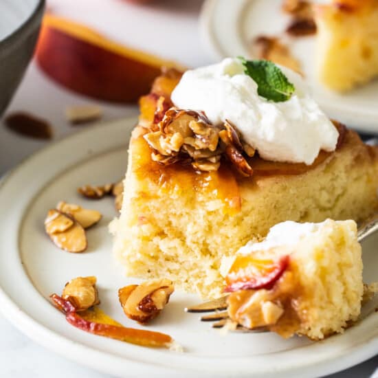 a slice of peach cake with whipped cream and almonds on a plate.