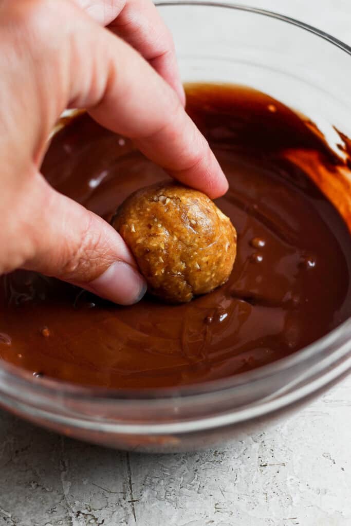 a person dipping a donut in chocolate sauce.