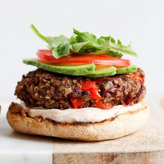 a black bean burger with lettuce, tomatoes and avocado on a cutting board.
