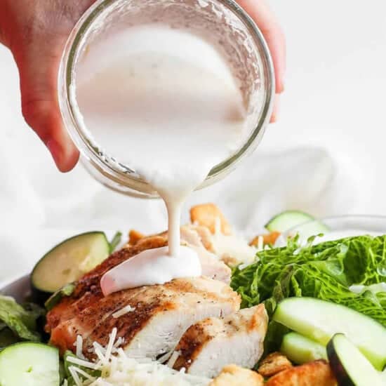 A person pouring a dressing over a salad.