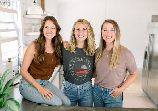 Tre fit foodie kvinner poserer for et bilde på et kjøkken.