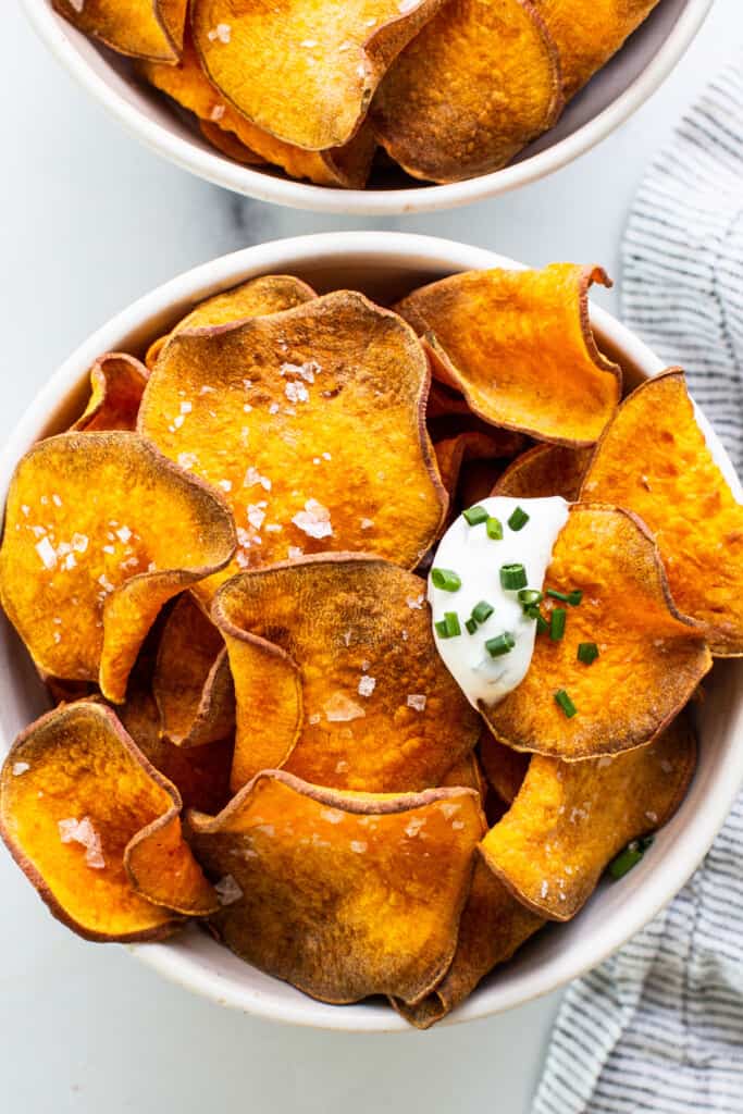 Two bowls of sweet potato chips with sour cream and chives.