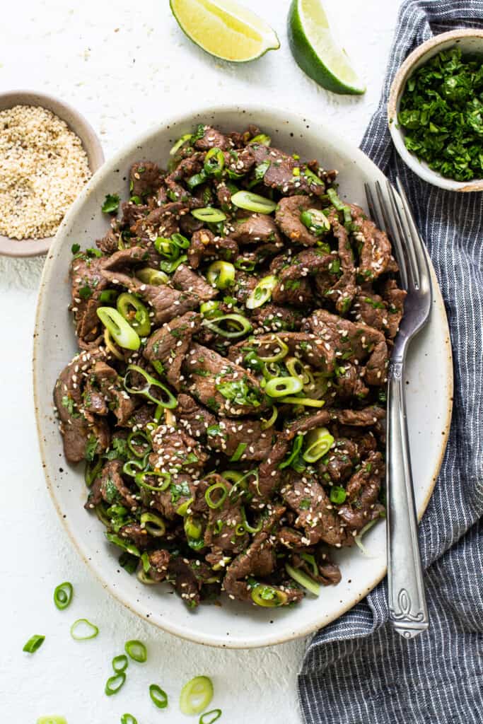 A bowl of beef with sesame seeds and green onions.