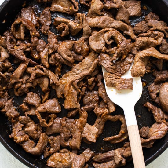 Beef in a skillet with a wooden spoon.