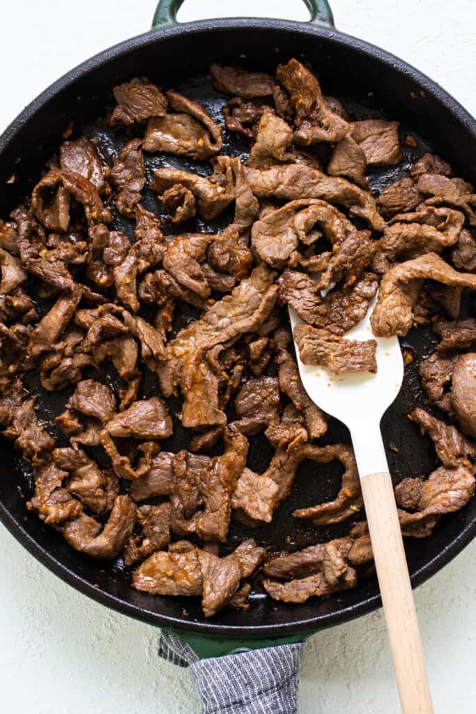 Beef in a skillet with a wooden spoon.