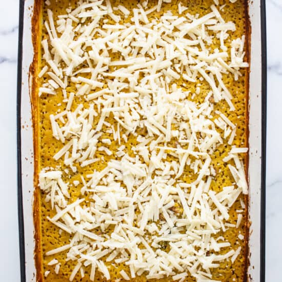 A white baking dish with a layer of cheese on top.