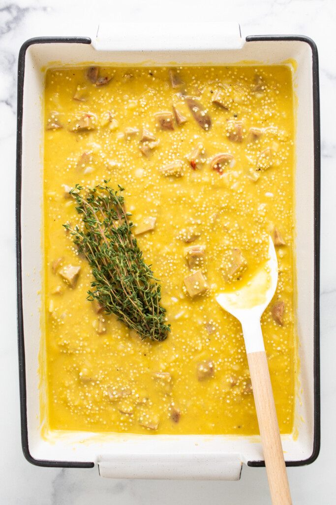 A bowl of soup with a spoon and a sprig of thyme.