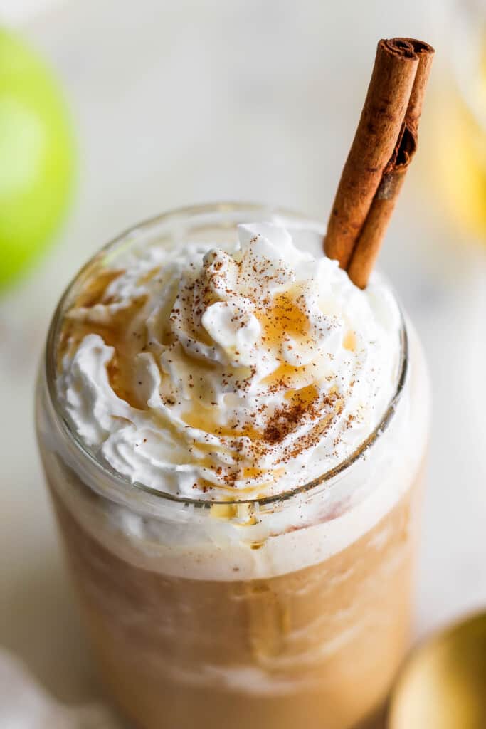 An apple latte with whipped cream and a cinnamon stick.