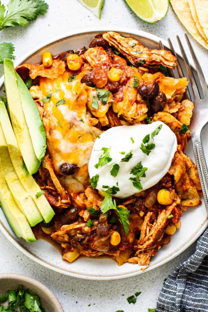 Mexican chicken enchilada on a plate with sour cream and avocado.