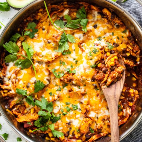 Chicken enchilada casserole in a pan with a wooden spoon.