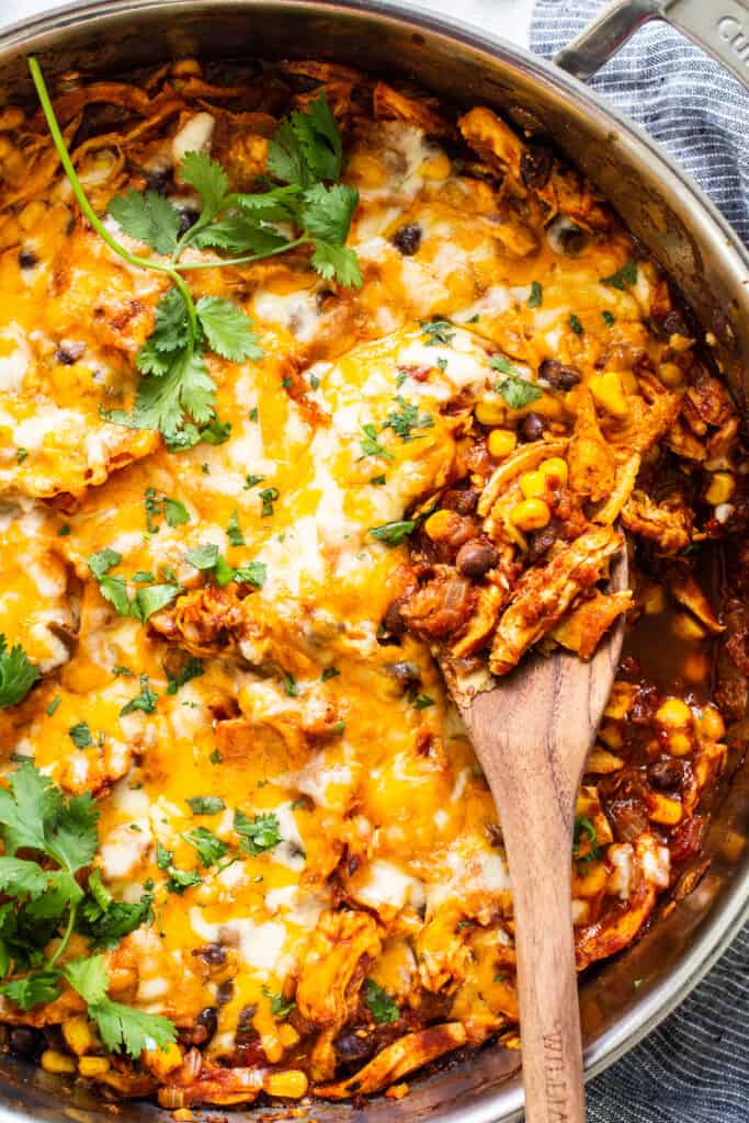 Mexican chicken enchilada in a pan with a wooden spoon.