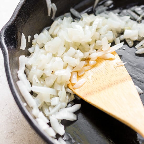 A frying pan with onions and a wooden spoon.