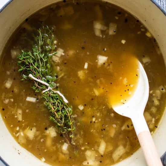 A pot of soup with a spoon and a sprig of thyme.