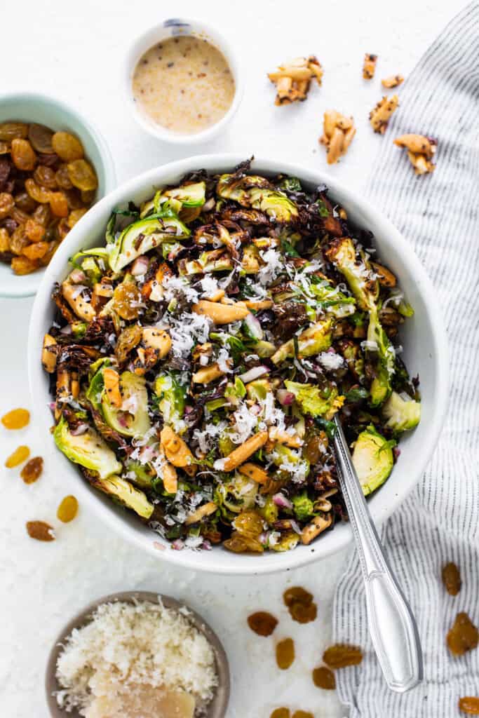 A bowl of brussels sprouts salad with nuts and raisins.