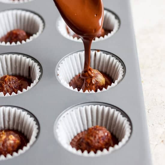 En skje drysser sjokolade over cupcakes i en muffinsform.