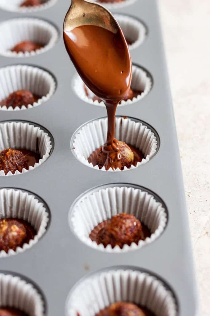 En skje drysser sjokolade over cupcakes i en muffinsform.