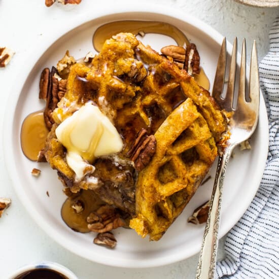 Pumpkin waffles with butter and pecans on a plate.