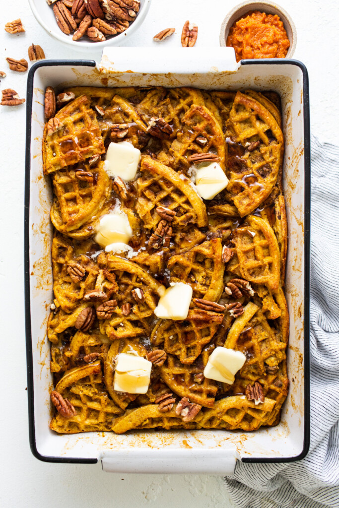 Pumpkin waffles in a baking dish with butter and pecans.