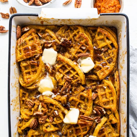 Pumpkin waffles in a baking dish with butter and pecans.
