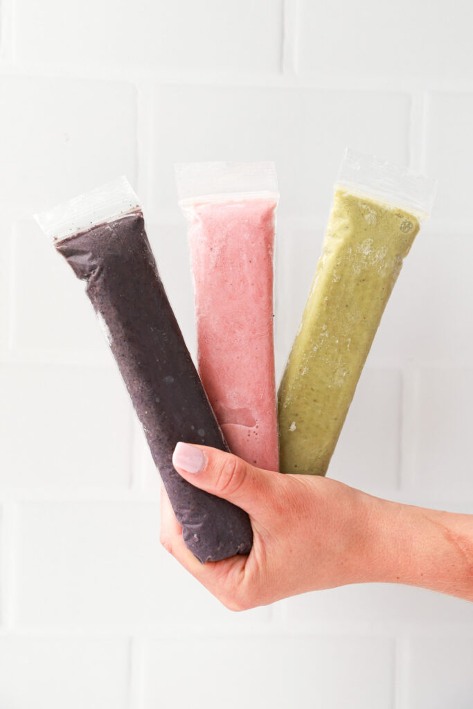 A hand ،lding three frozen popsicles.