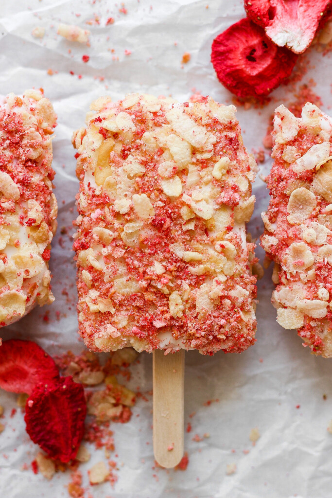 Three popsicles with strawberries and almonds on them.