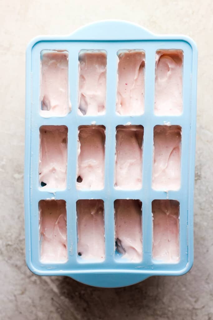 A blue ice cube tray filled with pink ice cream.