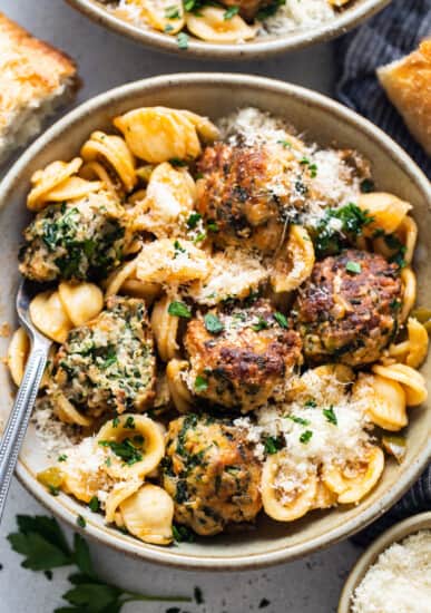 A bowl of pasta with meatballs and parmesan.