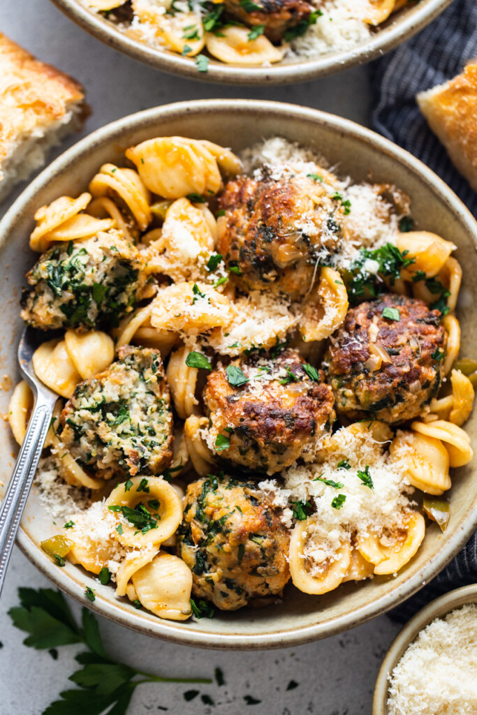 A bowl of pasta with meatballs and parmesan.