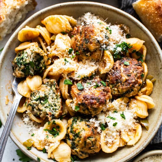 A bowl of pasta with meatballs and spinach.