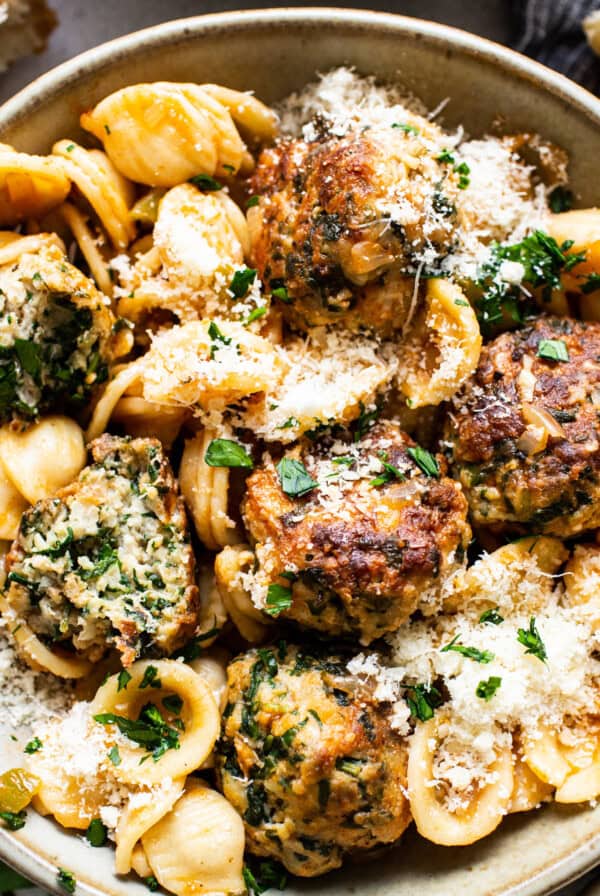 A bowl of pasta with meatballs and spinach.