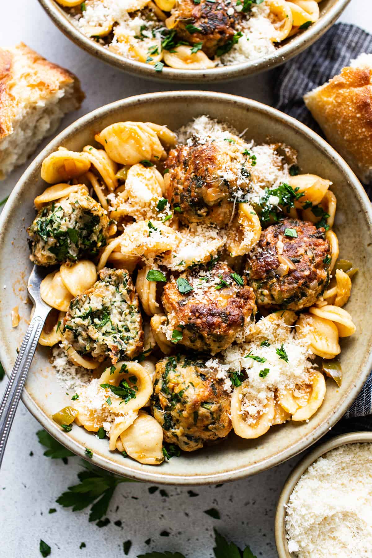 A bowl of pasta with meatballs and parmesan.