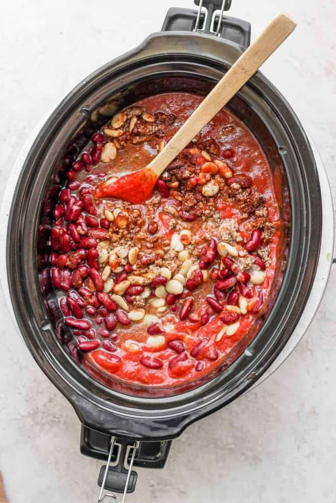A slow cooker turkey chili simmering with a wooden spoon.