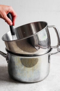 A person using a spatula to stir ingredients in a stainless steel pot.