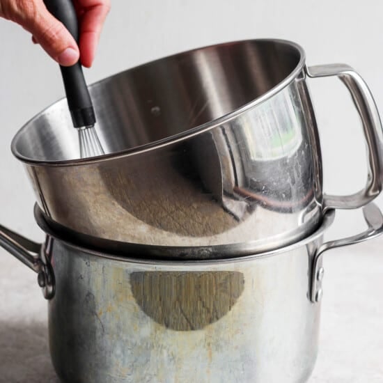 A person using a spatula to stir ingredients in a stainless steel pot.