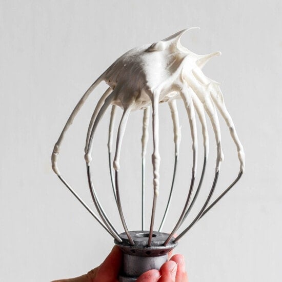 A person holding a whisk with whipped cream on it.