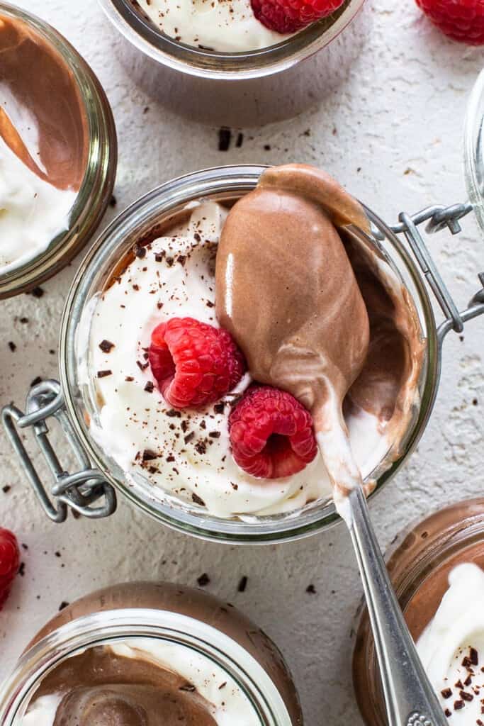 Chocolate mousse in jars with whipped cream and raspberries.