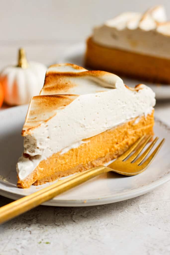 A slice of pumpkin pie on a plate with a gold fork.