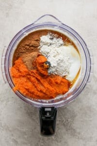 A food processor filled with ingredients for a pumpkin pie.