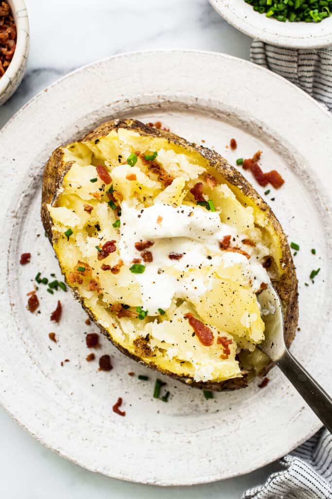 A baked potato with bacon and sour cream on a plate.