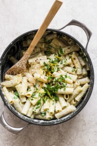 Penne pasta in a skillet with parmesan cheese and parsley.