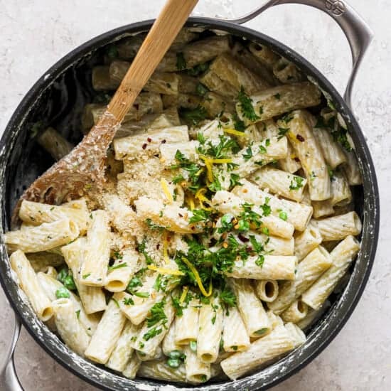 Penne pasta in a skillet with parmesan cheese and parsley.