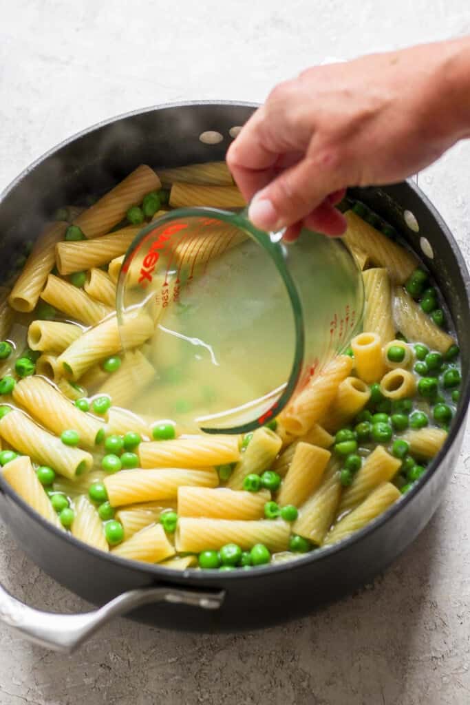 A person pouring pasta and peas into a pan.
