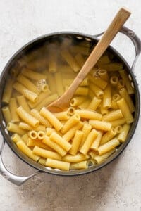 Penne pasta in a pan with a wooden spoon.