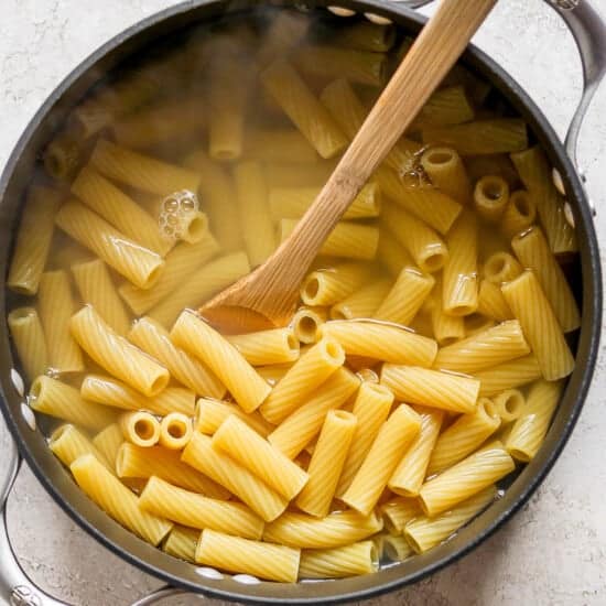 Penne pasta in a pan with a wooden spoon.