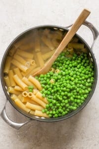 Peas and pasta in a pan with a wooden spoon.