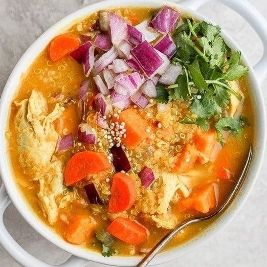 A bowl of chicken curry soup with carrots and onions.