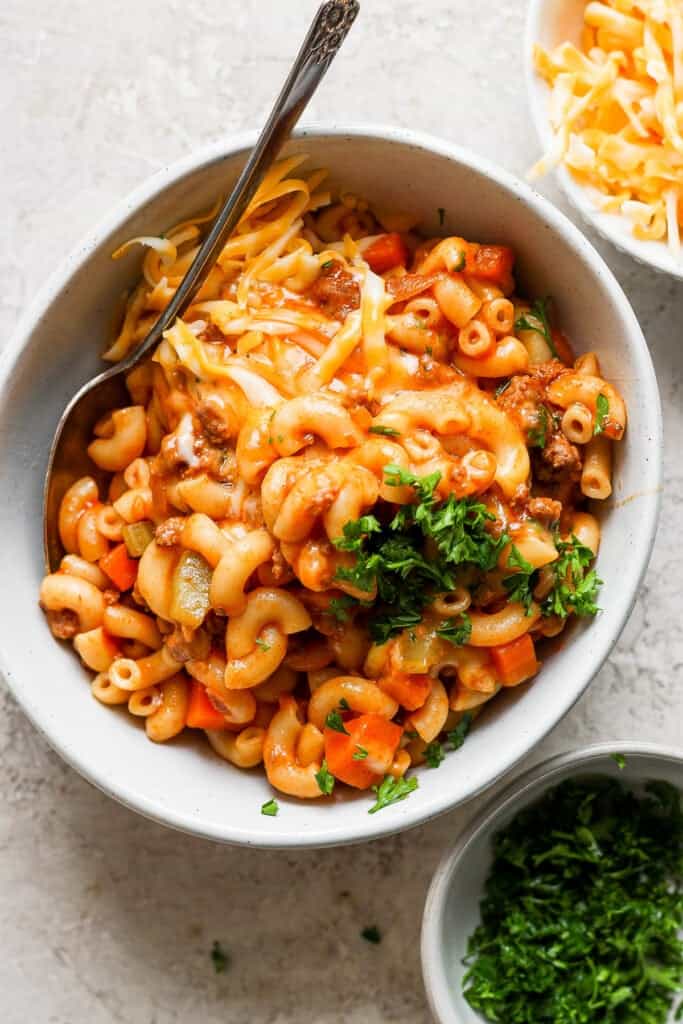 A bowl of macaroni and cheese with carrots and parsley.
