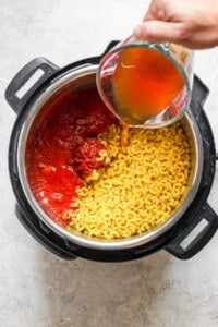 A person pouring sauce into a pot of pasta.